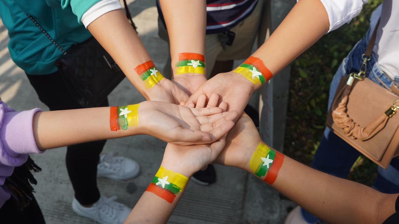 Volunteers showing unity with Myanmar flag wristbands, hands joined together in solidarity